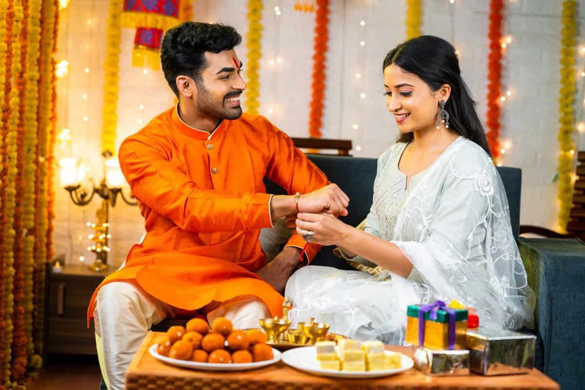 भाई अपनी बहन से राखी बंधवा रहा है और दोनों खुश होकर मुस्कुरा रहे हैं – रक्षाबंधन